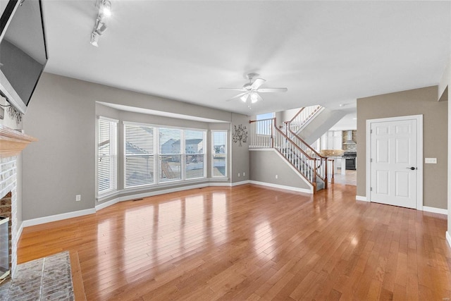 unfurnished living room with light wood-style floors, a fireplace, stairway, and ceiling fan