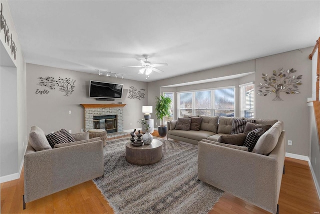 living room featuring light wood-style flooring, a fireplace, baseboards, and ceiling fan