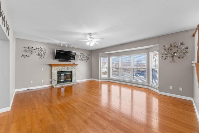 unfurnished living room with light wood-style flooring, a fireplace, baseboards, and a ceiling fan