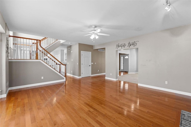 unfurnished living room with light wood finished floors, baseboards, stairway, and ceiling fan