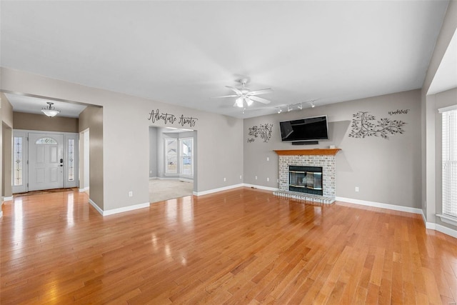 unfurnished living room with light wood-type flooring, a brick fireplace, baseboards, and a ceiling fan