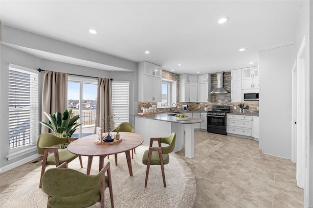 kitchen with tasteful backsplash, white cabinetry, a sink, gas range, and wall chimney exhaust hood