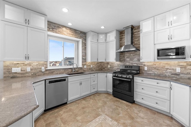 kitchen featuring stainless steel appliances, a sink, white cabinetry, backsplash, and wall chimney exhaust hood