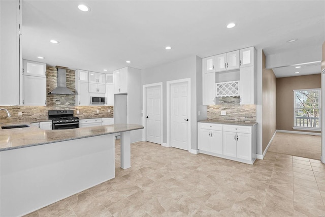 kitchen with light stone counters, stainless steel appliances, wall chimney range hood, white cabinetry, and a sink