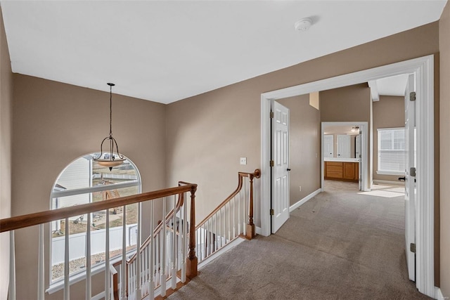 hallway featuring carpet floors, baseboards, and an upstairs landing