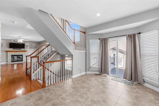 entrance foyer featuring a ceiling fan, a fireplace, stairway, and baseboards