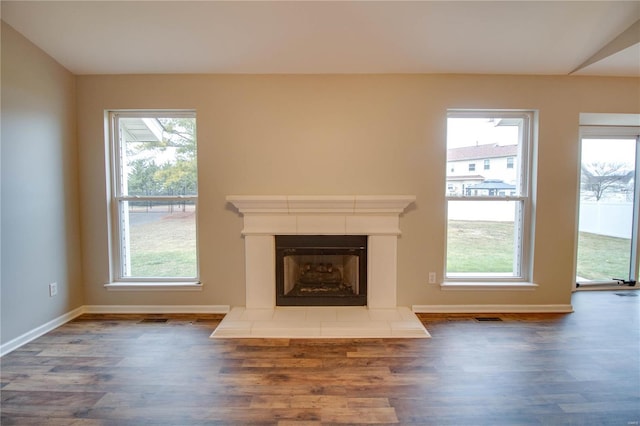 unfurnished living room featuring a tiled fireplace, plenty of natural light, and dark hardwood / wood-style floors