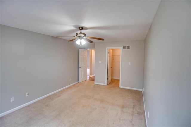 unfurnished bedroom with light carpet, a walk in closet, a closet, and ceiling fan