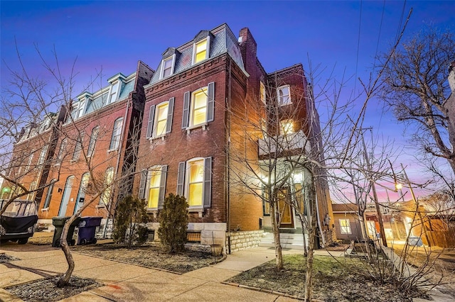 view of front facade with mansard roof, a high end roof, and brick siding