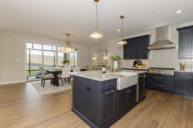 kitchen with dark cabinets, a center island with sink, appliances with stainless steel finishes, and wall chimney exhaust hood