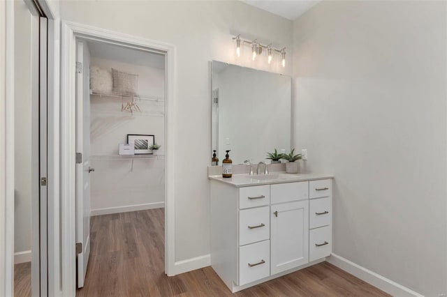 bathroom with wood finished floors, a walk in closet, vanity, and baseboards