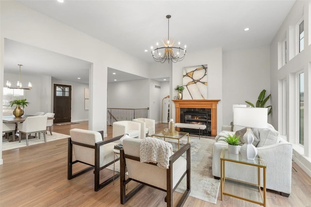 living area with a notable chandelier, light wood finished floors, recessed lighting, a glass covered fireplace, and baseboards