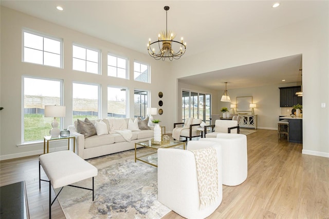 living room featuring a notable chandelier, light wood finished floors, recessed lighting, a high ceiling, and baseboards