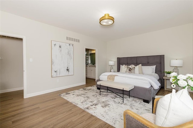 bedroom featuring light wood-style floors, baseboards, visible vents, and connected bathroom