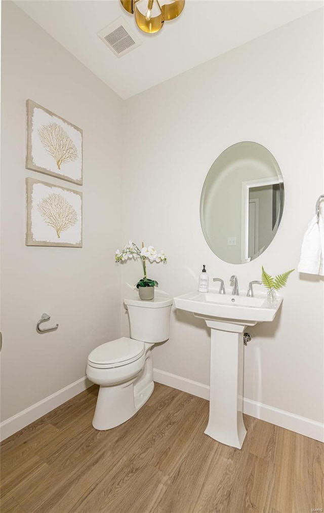 bathroom with baseboards, visible vents, toilet, and wood finished floors