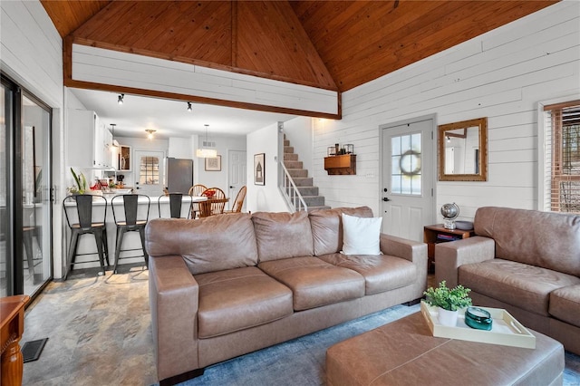 living room with high vaulted ceiling, wood walls, wood ceiling, visible vents, and stairway