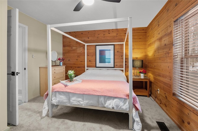 carpeted bedroom with ceiling fan, visible vents, and wooden walls