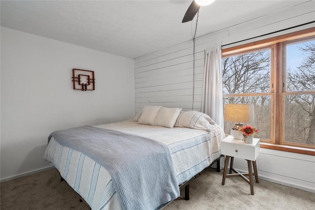 bedroom featuring carpet floors, ceiling fan, wooden walls, and baseboards