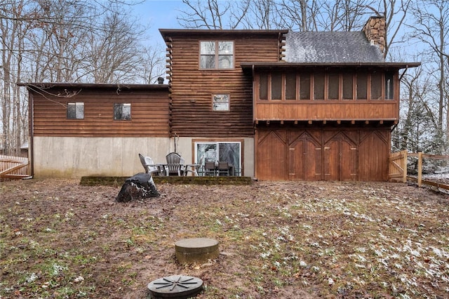 rear view of property with a chimney, log siding, and fence