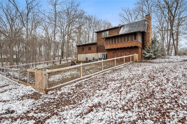 view of snow covered exterior featuring a chimney, fence, and log siding