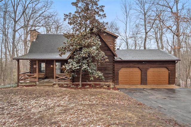 cabin with an attached garage, covered porch, aphalt driveway, and log exterior