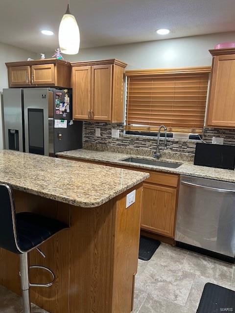 kitchen with a sink, stainless steel appliances, a kitchen bar, pendant lighting, and backsplash