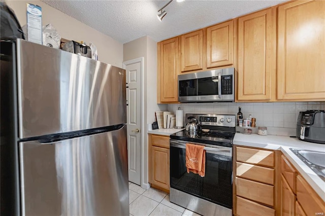 kitchen featuring appliances with stainless steel finishes, decorative backsplash, light tile patterned floors, light brown cabinets, and a textured ceiling