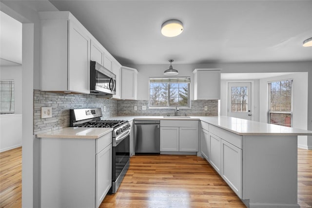 kitchen with sink, appliances with stainless steel finishes, white cabinets, decorative light fixtures, and kitchen peninsula