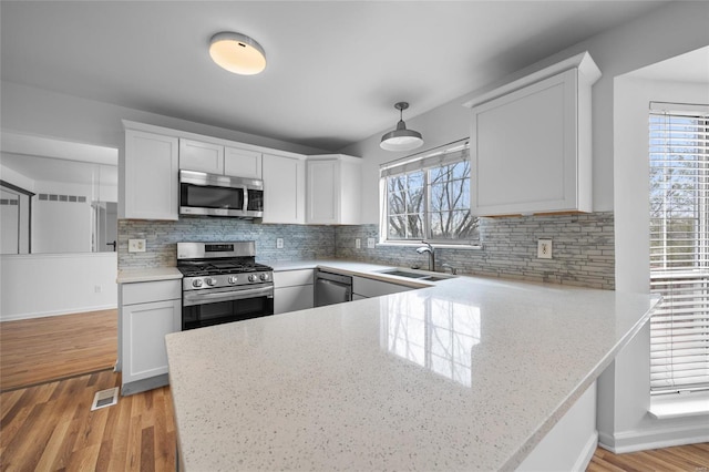 kitchen with pendant lighting, sink, white cabinets, stainless steel appliances, and light hardwood / wood-style flooring