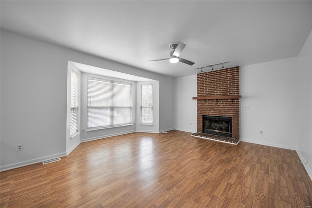 unfurnished living room featuring wood-type flooring, a brick fireplace, ceiling fan, and rail lighting