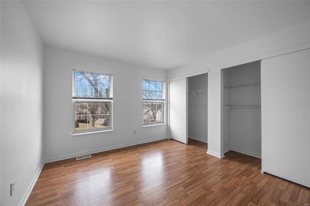 unfurnished bedroom with wood-type flooring and multiple closets