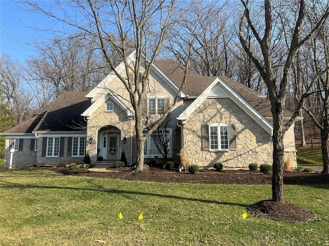 traditional-style home with stone siding, a front yard, and roof with shingles