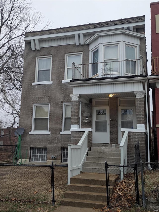 view of property featuring a porch, a fenced front yard, a balcony, brick siding, and a gate