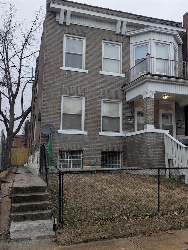 view of front of house with brick siding, a fenced front yard, and a balcony