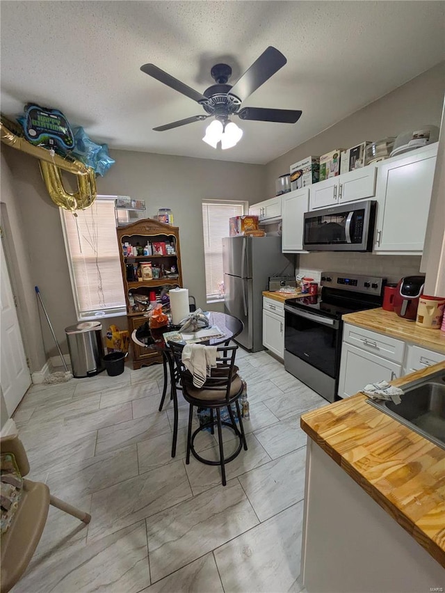 kitchen featuring white cabinets, butcher block countertops, stainless steel appliances, a textured ceiling, and a sink