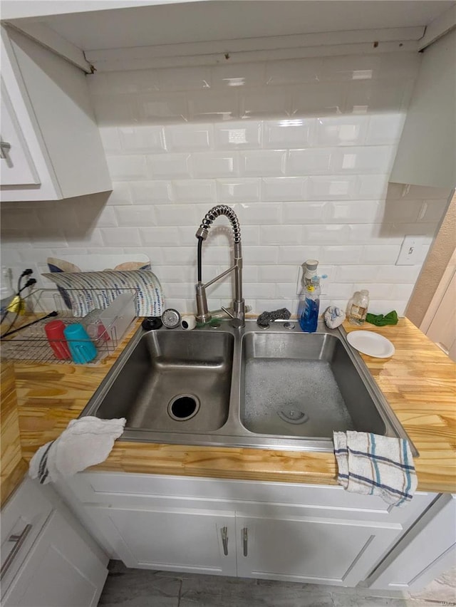 room details featuring wood counters, a sink, white cabinets, and decorative backsplash