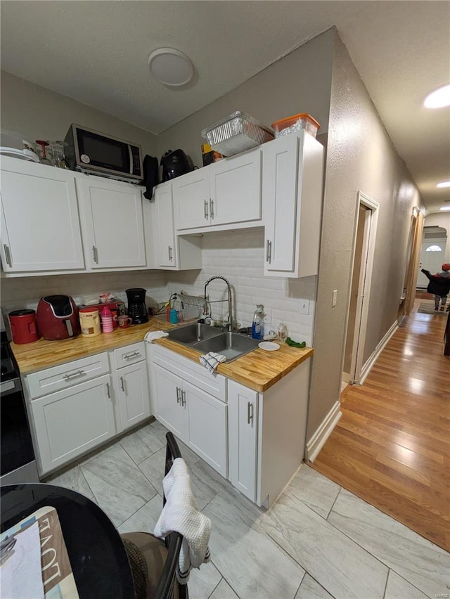 kitchen featuring light wood finished floors, butcher block counters, a sink, white cabinetry, and backsplash