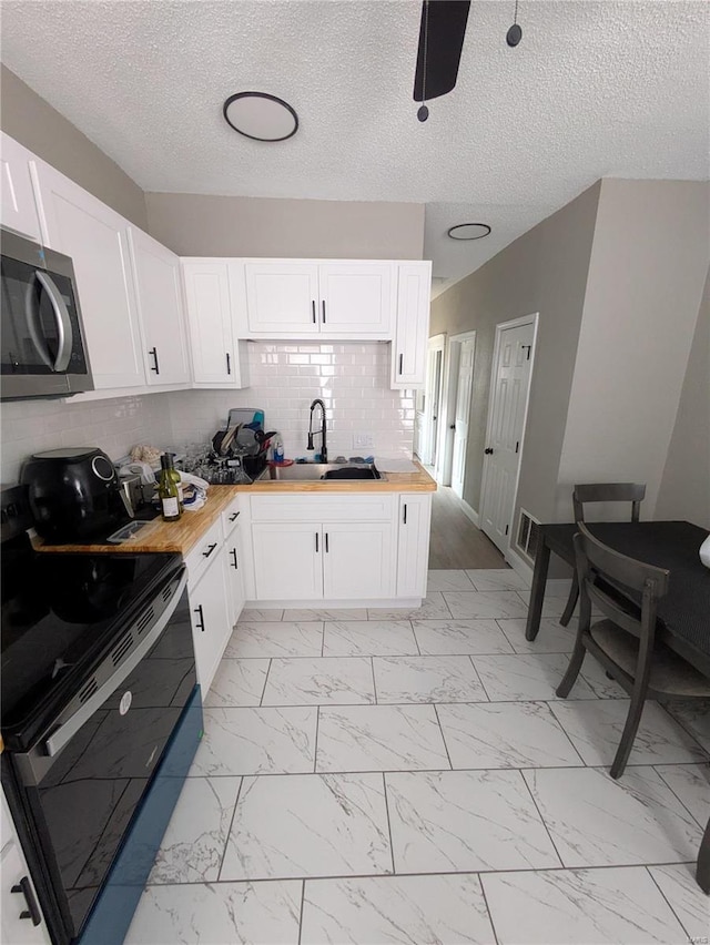 kitchen featuring black electric range, marble finish floor, butcher block counters, stainless steel microwave, and a sink