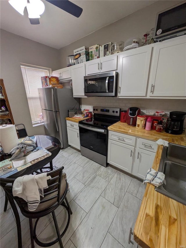 kitchen with a sink, butcher block counters, stainless steel appliances, and a ceiling fan