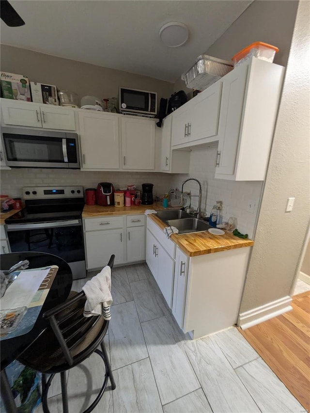 kitchen with stainless steel microwave, electric range, decorative backsplash, white cabinetry, and a sink