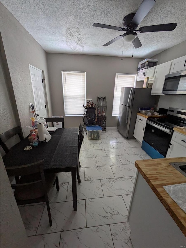 kitchen with marble finish floor, appliances with stainless steel finishes, white cabinets, and a textured ceiling