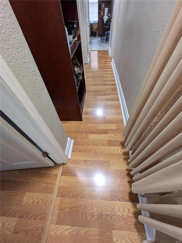 hallway featuring a textured wall, light wood-style flooring, and baseboards