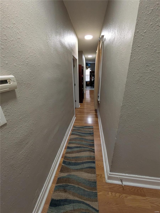 hall featuring a textured wall, wood finished floors, and baseboards