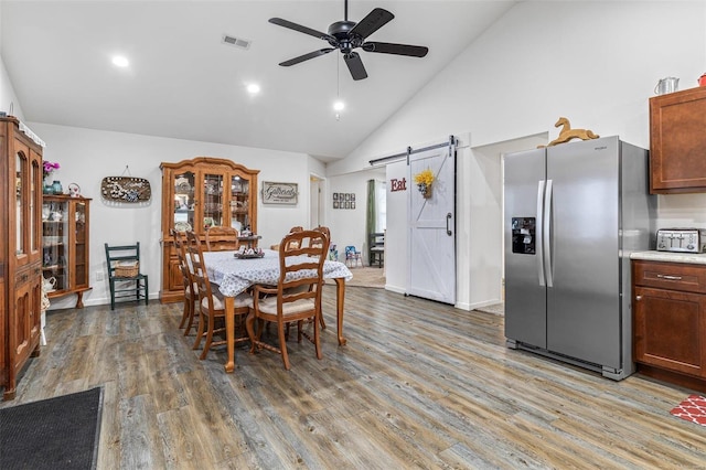 dining area featuring ceiling fan, wood-type flooring, a barn door, and high vaulted ceiling