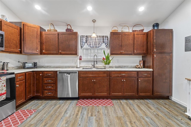 kitchen with pendant lighting, stainless steel appliances, sink, and light wood-type flooring