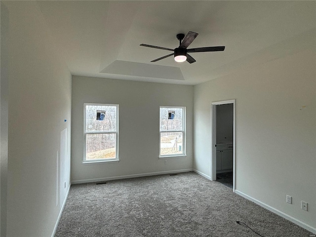 carpeted empty room featuring ceiling fan and a raised ceiling