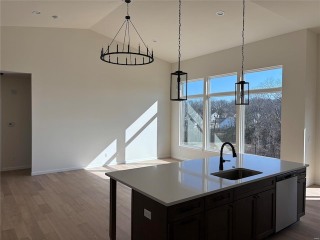 kitchen featuring light countertops, vaulted ceiling, stainless steel dishwasher, wood finished floors, and a sink