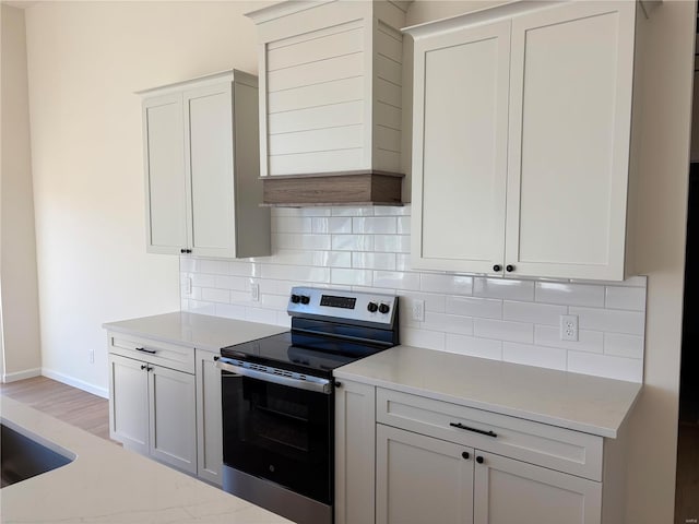 kitchen with electric range, light stone countertops, baseboards, and backsplash