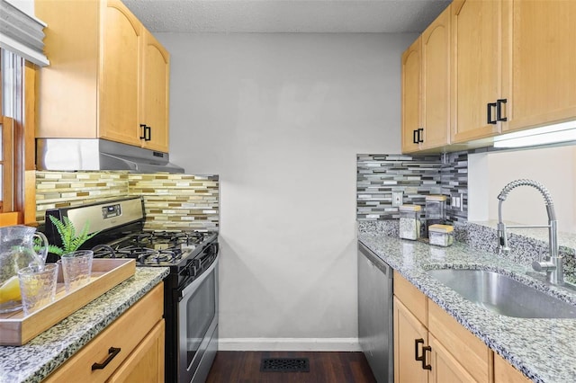 kitchen featuring light stone countertops, baseboards, a sink, under cabinet range hood, and appliances with stainless steel finishes