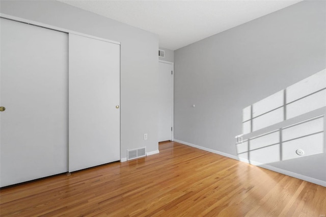 unfurnished bedroom with a closet, visible vents, baseboards, and wood finished floors